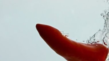 Kırmızı biberli su sıçratıyor. Şeffaf sıvıda akan baharatlı sebze yıkama. Taze kırmızı biber kabarcıklar halinde yükseliyor. Lezzetli salata malzemesi. Çiğ sağlıklı yeme konsepti