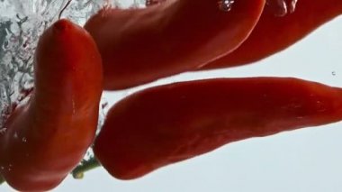 Chili biberleri arka planda hafif çekimde su düşürür. Lezzetli organik sebzeler, şeffaf sıvının içinde kıvrılırlar. Pişirmek için baharatlı kırmızı malzeme. Çiğ vejetaryen sağlıklı beslenme konsepti.