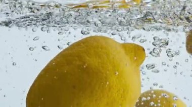 Tropik limonlar su sıçratıyor. Sarı ekşi meyveler şeffaf sıvıyla zıplıyor. Yaz tazeleyici kokteyl için lezzetli narenciye. Yemek şovu reklamı. Vejetaryen sağlıklı beslenme konsepti.