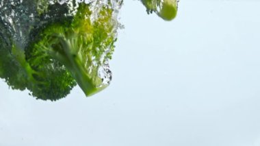 Şeffaf suda yüzen taze brokoli kümeleri ve kabarcıklar. Olgun yeşil sebze, berrak bir sıvının içine düşüyor ve çok yavaş sıçrıyor. Beyaz arka planda su altında vitamin sebzeleri