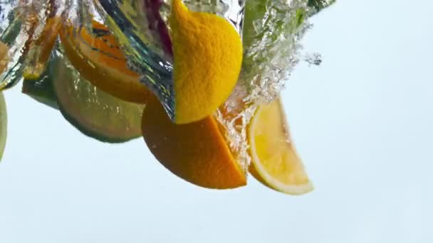 スライスされた様々な果物は 白い背景に透明な液体を閉じました 超遅い動きでレモネード落下水のための新鮮なおいしい成分 有機オレンジリンゴイチゴ水中 — ストック動画