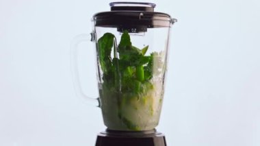 Elektrikli blender sebze smoothie 'sini süper yavaş çekimde hazırlıyor. Yeşil organik sebzeler, meyve karıştırıcı cam kasenin içine karıştırılmış beyaz arka plan. Sağlıklı vejetaryen kokteyli..