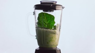 Elektrikli blender, sebze meyvelerini karıştırarak vitamin kokteylini süper yavaş çekimde hazırlıyor. Beyaz arka planda cam kasenin içine karıştırılmış taze ham maddeler. Vejetaryen yemeği pişirmek.