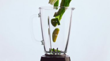 Yeşil sebzeli cam blender kaseye çok yavaş düşüyor. Taze vitamin sebzeleri, beyaz arka planda meyve karıştırıcısı. Sağlıklı yaşam tarzı için lezzetli organik yiyecekler..