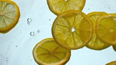 Beyaz arka planda su altında taze parlak limonlar. Sarı narenciye dilimleri suyun altında çok yavaş bir şekilde kabarcıklarla yüzüyor. Tazeleyici içecek için lezzetli vitamin bileşeni.