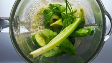 Sebzeleri cam karıştırıcı kaseye karıştıran üst manzara. Kapatın. Yeşil maydanozlu lahana avokado elmalı salatalık parçaları elektrikli mikserin içinde yavaş çekimde karıştırılmaya başlandı. Smoothie pişirme konsepti.