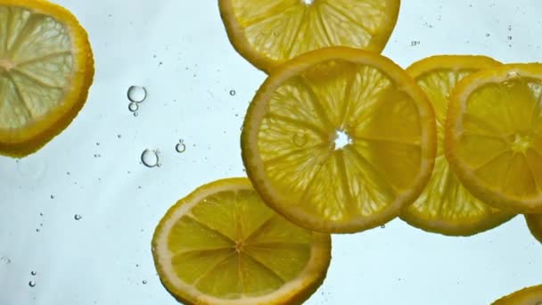 用白色的背景把新鲜明亮的柠檬放在水下 黄色的柑橘片漂浮在水下 水泡很深 运动非常缓慢 新鲜饮料的味觉维生素成份 — 图库视频影像