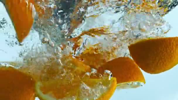 新鮮なジューシーなオレンジのウェッジは 超遅い動きで澄んだ水の下に沈んで飛び散って閉じます 明るいおいしい柑橘類の作品は白い背景に水中に落ちた 泡で浮かぶビタミンフルーツ — ストック動画