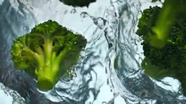 Yeşil çiğ brokoli beyaz zemin üzerine şeffaf su düşürdü. Olgun vitamin lahanası, berrak sıvının içine düşerek kabarcıklar oluşturur. Süper yavaş çekimde yüzen organik sebzeler.