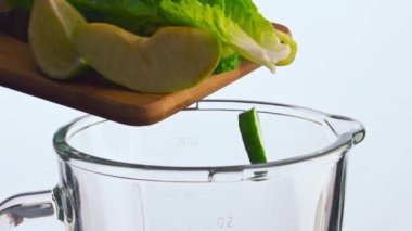 Çeşitli meyve sebzeleri ahşap tahtadan blender kasesine yakın mesafeden düşer. Taze sebzeler cam karışımına süper yavaş çekimde düştü. Smoothie için lahana avokado elmalı salatalıklı kivi..