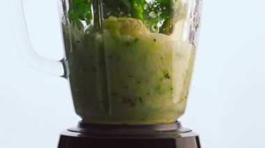 Cam kase karışımında taze yeşil sebzeleri süper yavaş çekimde karıştırıyorum. Beyaz arka planda çiğ sebze karışımı. Sağlıklı detoks smoothie için doğal organik bileşenler.