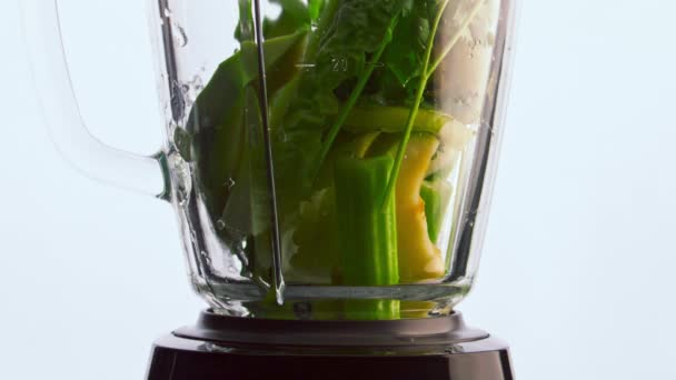 ブレンダーにスライスされた緑の野菜は 明確な水で閉じ注ぎました 有機おいしい野菜ガラスミキサーボウル白の背景にハーブ 超スローモーションでビタミンスムージーを準備 — ストック動画