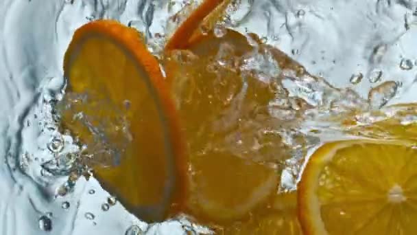 橙子片在超慢速运动的过程中以特快的速度掉进清澈的水中 鳞片多汁柑橘类水果溅在透明的泡沫水的白色背景 新鲜果汁的味觉维生素成份 — 图库视频影像