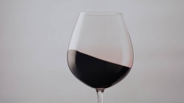 Beyaz arka planda cam kadehte güzel bir kırmızı şarap dalgası var. Şeffaf şarap kadehinde dönen lezzetli bordo alkollü içecek süper yavaş çekimde. Cabernet yüzeyi kristal bardakta dalgalanır..
