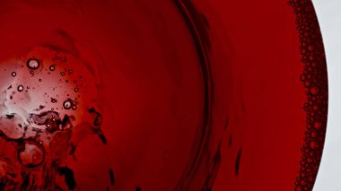 Alkollü içecek kadehini yakın çekim için dolduruyorum. Temiz şarap kadehini dolduran sarhoş edici kırmızı sıvı beyaz arka plan. Şarap, cam tabanda dalgalar oluşturur. Gül rengi jet hızla su sıçratıyor şeffaf camlar