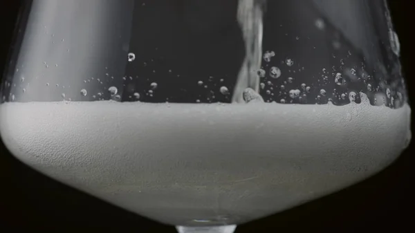 Golden fizzy beverage bubbling pouring into glass goblet in super slow motion close up. Bubbles foam raising over champagne surface on black background. Sparkling tasty alcohol drink for celebration.