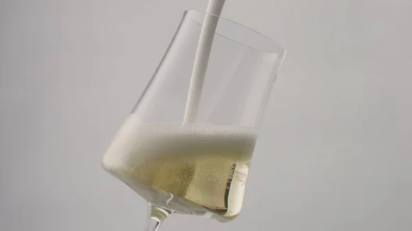 Stream champagne foam pouring to glass goblet in super slow motion close up. Golden sparkling wine flowing elegant wineglass on white background. Alcohol bubbly drink foaming in transparent glassware.