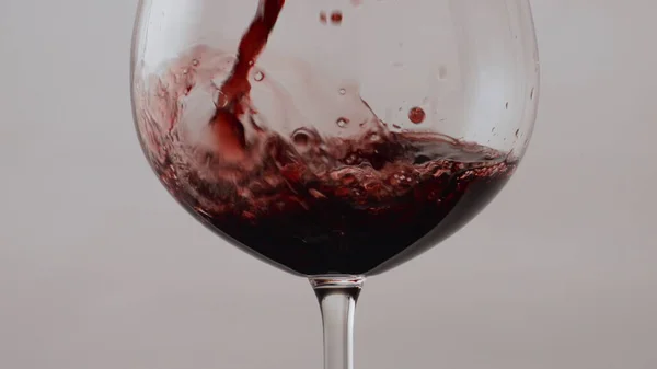 超スローモーションでクリスタルガラスのゴブレットにローズワインを注ぐが閉じます 透明なワイングラスに流れる赤いメルロをストリームします ブルゴーニュアルコール飲料白を背景にガラスの中に泡立つ — ストック写真