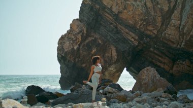 Yogi kadın poz dansçısı. Kayalık deniz kıyısında yaz günü yoga yapıyor. Afrika kökenli Amerikalı sporcu tek bacaklı denge esnekliği eğitimi alıyor. Sağlıklı vücut kavramı.