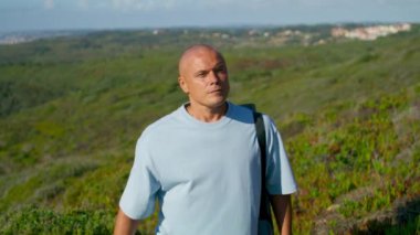 Turistler güneş ışığında yeşil uçurum kenarında okyanus manzarasında yürürler. Odaklanmış adam yoga minderini tutuyor deniz kıyısındaki antrenman yerini seçiyor. Atletik adam deniz manzarası seyrediyor açık havada dinleniyor. Sakin insanlar konsepti.