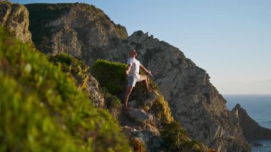Muhteşem okyanus uçurumu manzarasında yoga yapan bir adam. Odaklanmış atlet egzersizi akşam güneşinde doğa evreniyle ruhsal bağlantı kuruyor. Zen dağ kenarı kavramındaki ahenk gibidir..