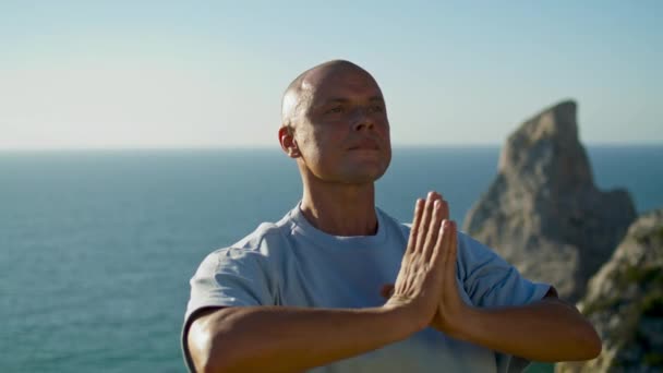 运动员练习瑜伽 看大海 专注的人在美丽的海崖边缘以令人惊艳的姿势沉思 秃头英俊的小伙子在室外阳光下做运动 集中精神的概念 — 图库视频影像