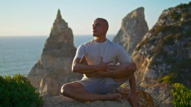 Güneş ışığında yoga yapan yakışıklı bir adam güzel bir okyanus kayası. Odaklanmış güçlü bir sporcu nefes kesici doğada çalıştıktan sonra rahatlar. Huzurlu adam deniz kıyısında dinleniyor. Yaşam tarzı konsepti gibi.