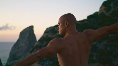 Kaslı adam akşam okyanusta üstsüz antrenman yapıyor. Uçuruma odaklanmış yoga. Huzurlu Yogi meditasyonunu sabah denizinde asana yaparak yap. Aktif zen yaşam tarzı gibi. İç uyum dengesi kavramı.