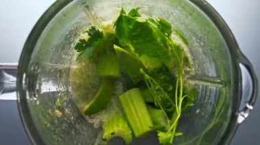 Elektrikli blender çiğ organik sebzelerle doldurulmuş taze vitamin smoothie 'sini süper yavaş çekimde hazırlıyor. Vejetaryen kokteyli için cam kaseye karıştırılmış sebze dilimleri..