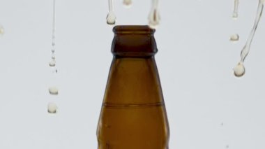 Süper yavaş çekimde açıldıktan sonra şişeden su sıçratan el yapımı altın bira. Sarı damlacıklar beyaz arka planda patlıyor. Kutlama yapmak için buğday aromalı alkol içeceği..