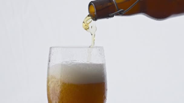 白い背景に透明なガラスに琥珀色のおいしいビールを注ぐ暗いボトルを閉じます ストリーム黄金のラガー新鮮な飲み物をクリアゴブレット泡泡超スローモーションを作るに流れる 醸造コンセプト — ストック動画