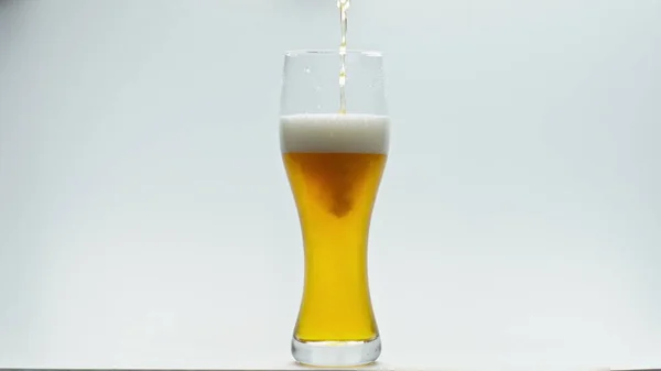 超スローモーションでクリスタルゴブレットを注ぐ軽い新鮮なビールが閉じます 白い背景に透明なガラスの中で泡立つホップ小麦アルコール飲料 リフレッシュのための醸造酒から準備ができている — ストック写真