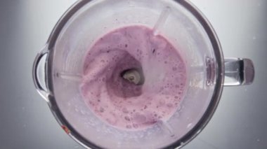 Ev yapımı böğürtlenli smoothie 'nin üst görüntüsü süper yavaş çekimde harmanlanıyor. Gri arka planda lezzetli meyveli süt içeceği karıştıran elektrikli blender. Kahvaltıda taze sütle yoğurt hazırlıyorum..