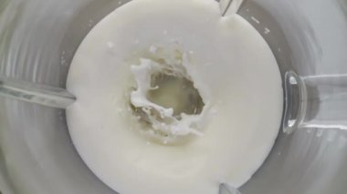 Elektrikli mikser organik taze sütü süper yavaş çekimde karıştırıyor. Cam karıştırma kabının içinde dönen beyaz süt ürünü. Milkshake yoğurt suyu için doğal protein bileşeni..