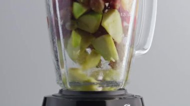 Meyve püresi karışımı için taze dilimlenmiş malzemeler cam karıştırıcı kasesinde çok yavaş çekimde harmanlanıyor. Lezzetli organik meyve blender içinde karıştırılmış beyaz arka planda. Vitamin yiyeceği hazırlıyorum..