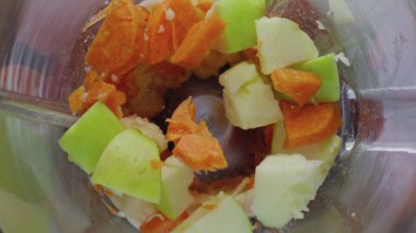 Blender cam kasesinin içinde taze lezzetli sebzeler doğranıyor. Hem de çok yavaş çekimde. Vitamin kokteyli için dilimlenmiş elma havucu ve muz karışımı. Sağlıklı beslenme.