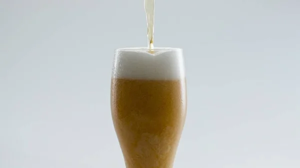 透明ガラスを超スローモーションで金色のビールで満たします ストリーム新鮮なラガーアルコール飲料白の背景に明確なゴブレットに注ぐ 泡状小麦麦芽飲料を覆う密な泡 — ストック写真