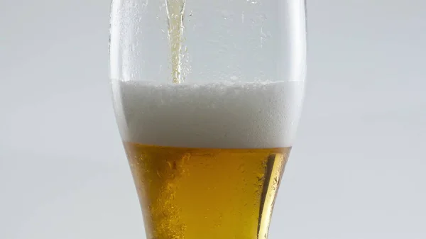 透明なガラスに注ぐ琥珀色のラガービールは 白い背景においしい濃い泡を作り出します 結晶ゴブレット超スローモーションに注ぐ黄金の小麦アルコール飲料 飲み物 — ストック写真