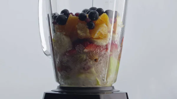 Electric blender blending tasty organic fruits berries with fresh water for natural vitamin cocktail close up. Sliced sweet ingredients mixing inside glass bowl in super slow motion. Healthy food.