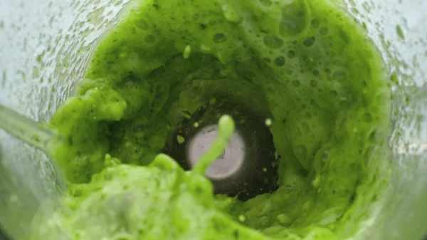 Green smoothie foaming bubbling in electric blender close up. Top view of fresh vitamin vegetable cocktail swirling inside glass bowl mixer in super slow motion. Detox cocktail for healthy nutrition.