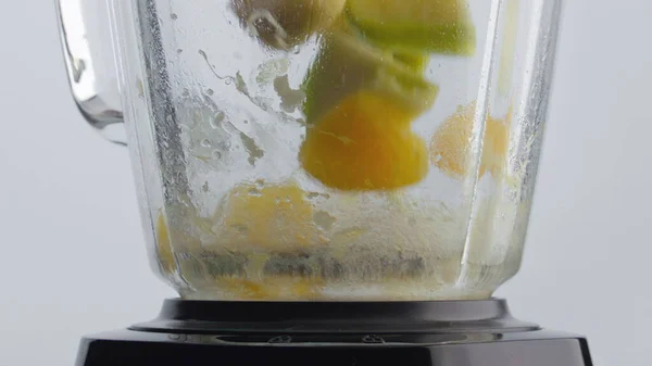 Chopping fresh tasty fruits in blender for making vegetarian food close up. Sliced colorful apple orange banana falling in mixer bowl super slow motion. Preparing vitamin antioxidant cocktail.