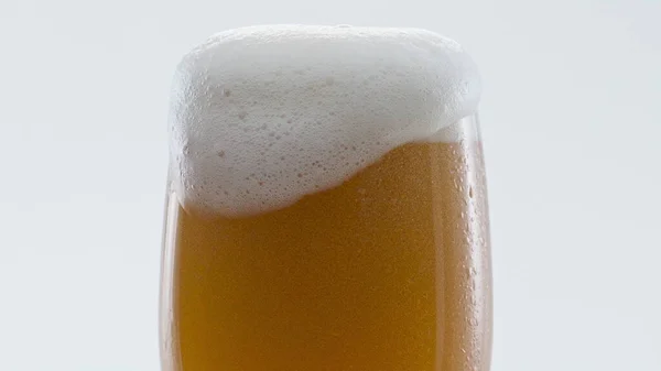 Closeup hoppy unfiltered beer foaming in glass super slow motion. Foam alcohol beverage flowing down clean goblet on white background. Fresh craft heady liquid bubbling in full transparent mug.