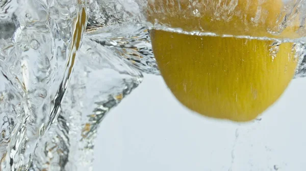 Yellow citrus drop water in light background closeup. Fresh sour lemons splash making swirl in light background. Tropical fruits falling transparent liquid. Organic food natural antioxidant concept.