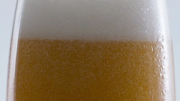 Amber beer white foam bubbling on edge glass at white background close up. Many bubbles swirling inside golden alcohol liquid in super slow motion. Lager wheat drink foaming in transparent goblet.