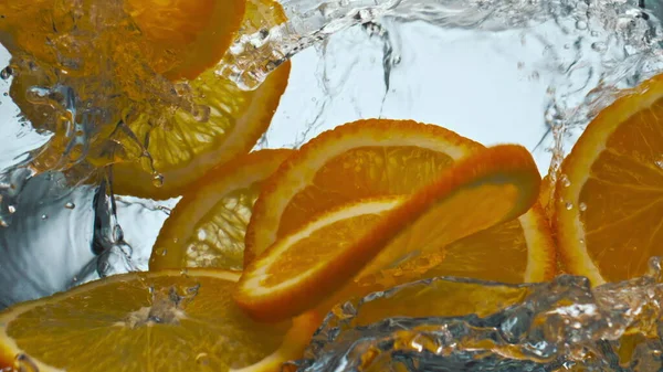 Bright slices tasty orange splashing transparent water in super slow motion close up. Vitamin fresh citrus falling clear liquid on white background. Delicious tropical ingredient for lemonade.