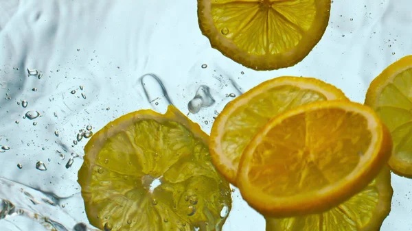 Sliced sour lemon falling clean water making splashes in super slow motion close up. Vitamin healthy citrus fruit floating transparent liquid on white background. Organic food for delicious drink.