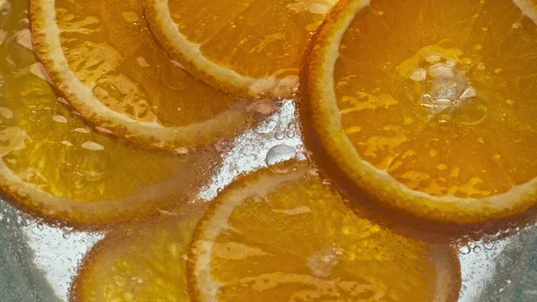 Closeup oranges fizzy water in light background. Refreshing citrus beverage lemonade bubbling in cup. Delicious tropical fruit pieces in soda drink. Beautiful summer party preparation commercial.