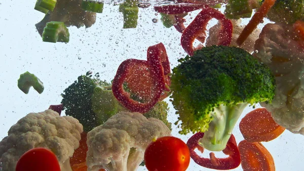 Closeup fresh veggies water floating in super slow motion. Colorful organic vegetables dropped transparent liquid on white background. Raw healthy ingredients for tasty salad. Vegetarian nutrition.