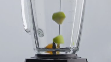 Taze parçalar meyve karıştırıcıyı süper yavaş çekimde yakın çekimde fırlatıyor. Dilimlenmiş portakallı elma cam karıştırıcı kasesine düşüyor. Smoothie kokteyli hazırlamak için vitamin organik sulu malzemeler ekliyorum..