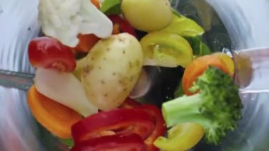 Elektrik mikserinin içinde çok yavaş çekimde harmanlanan farklı çiğ sebzeler. Detoks için organik renkli malzemelerin üst görüntüsü. Sağlıklı yaşam tarzı için vitamin besin.